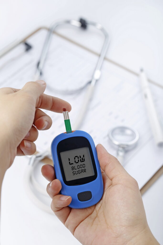 Mão segurando um medidor de glicose no sangue para medir o nível de açúcar no sangue, o fundo é um estetoscópio e um arquivo de gráfico